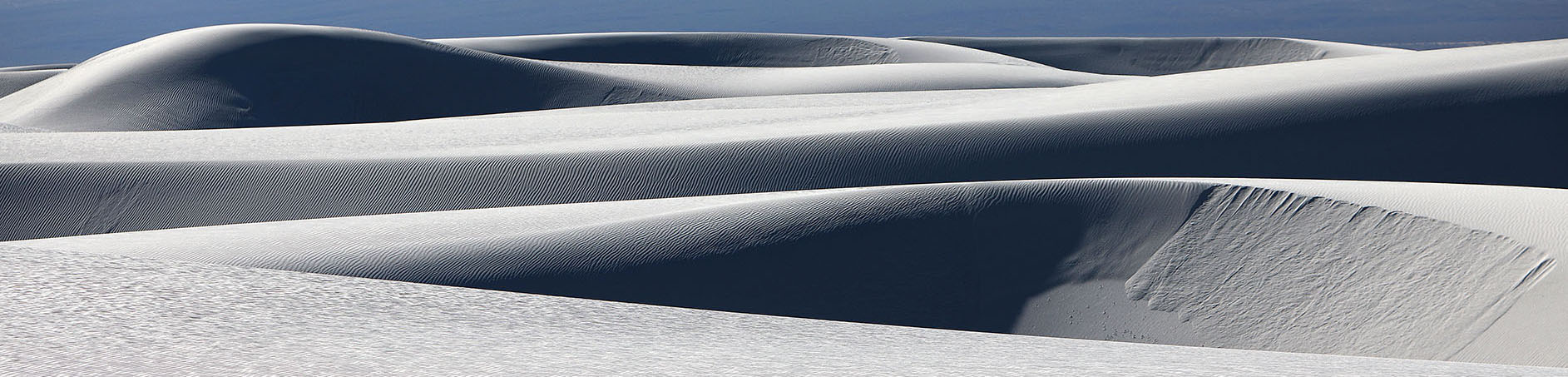 White sand dunes with rippled textures under a deep blue horizon